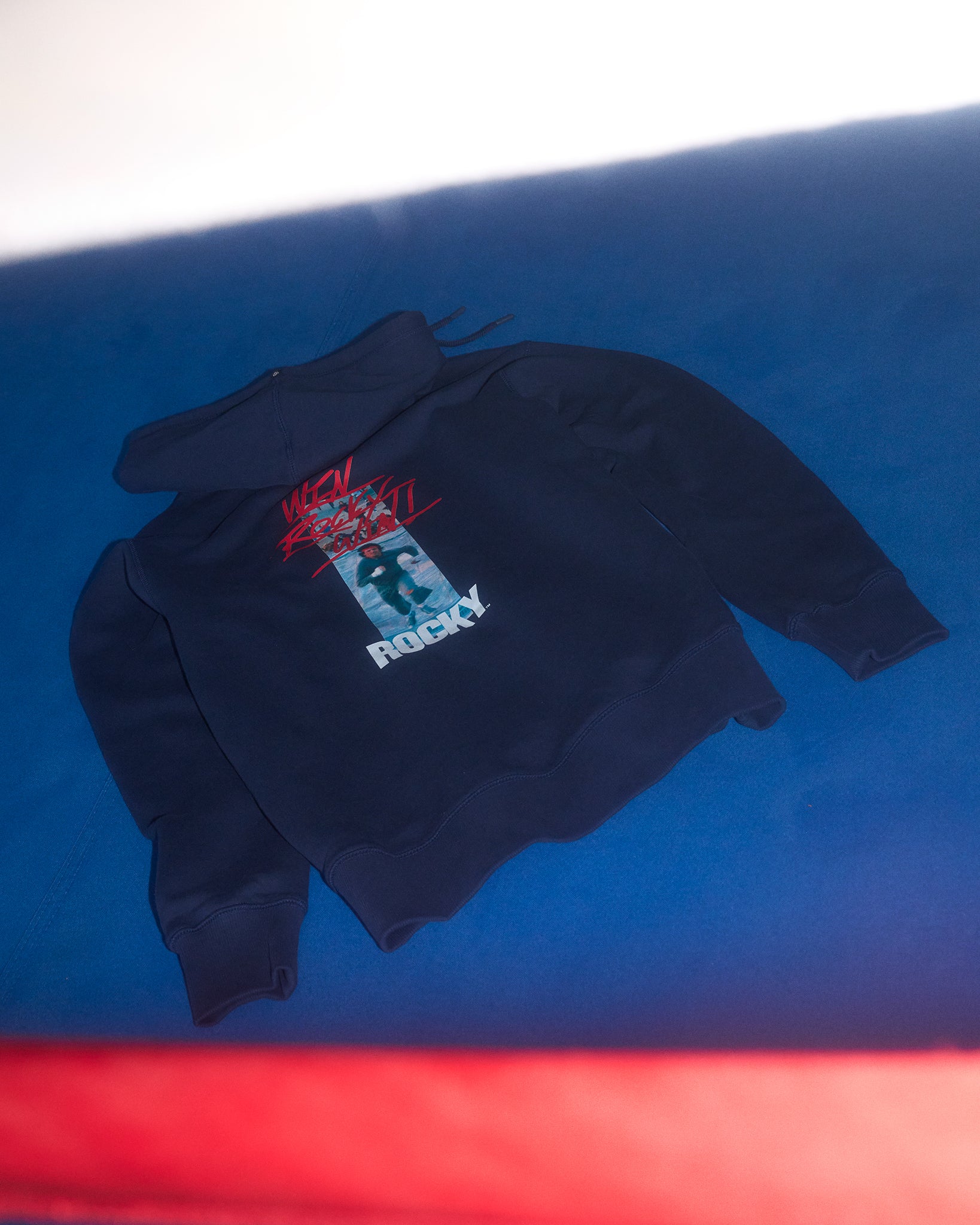 Folded black hoodie with 'Rocky' graphic on a blue surface