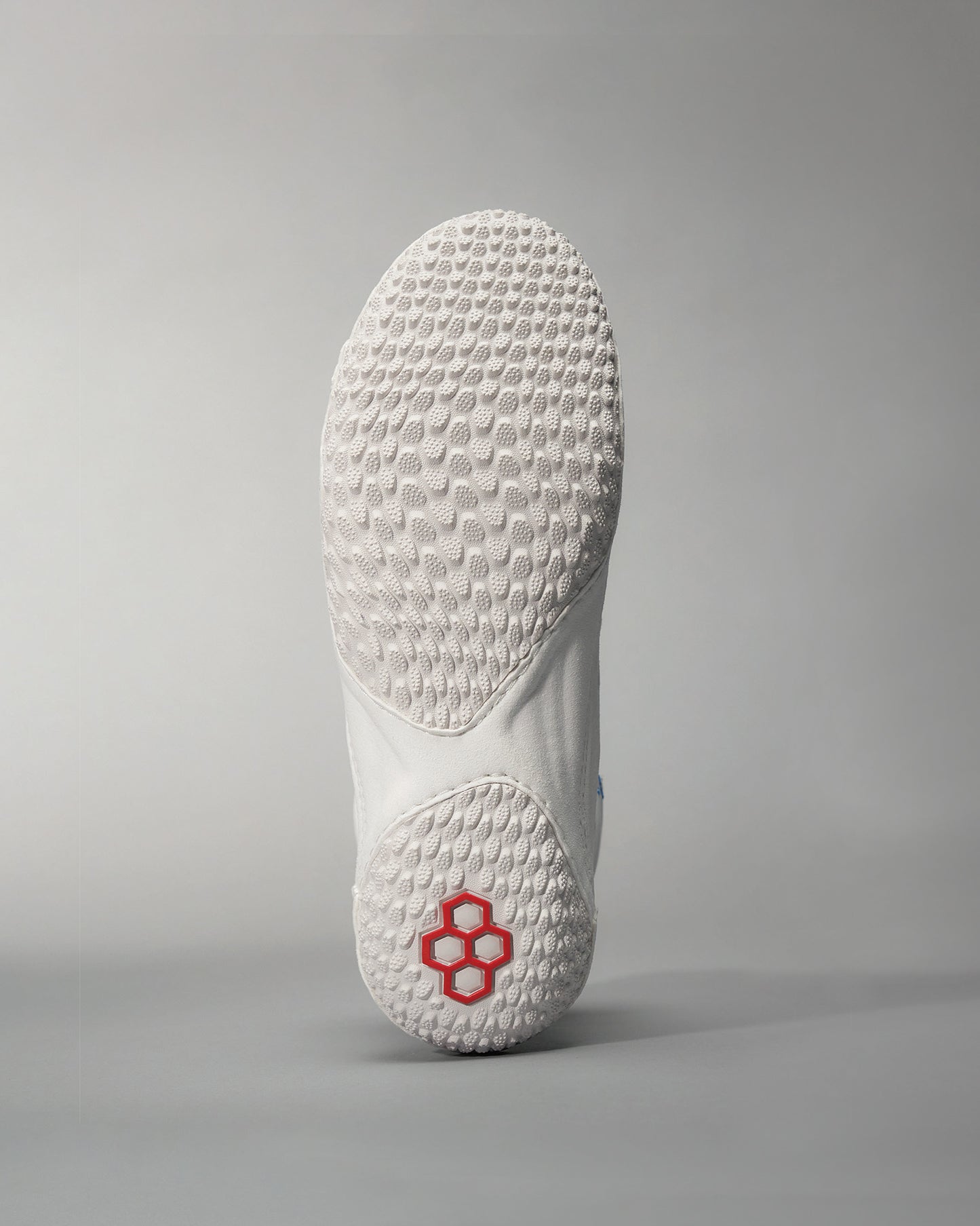 A close-up of the sole of a white athletic shoe featuring a unique textured pattern for grip and a striking red logo