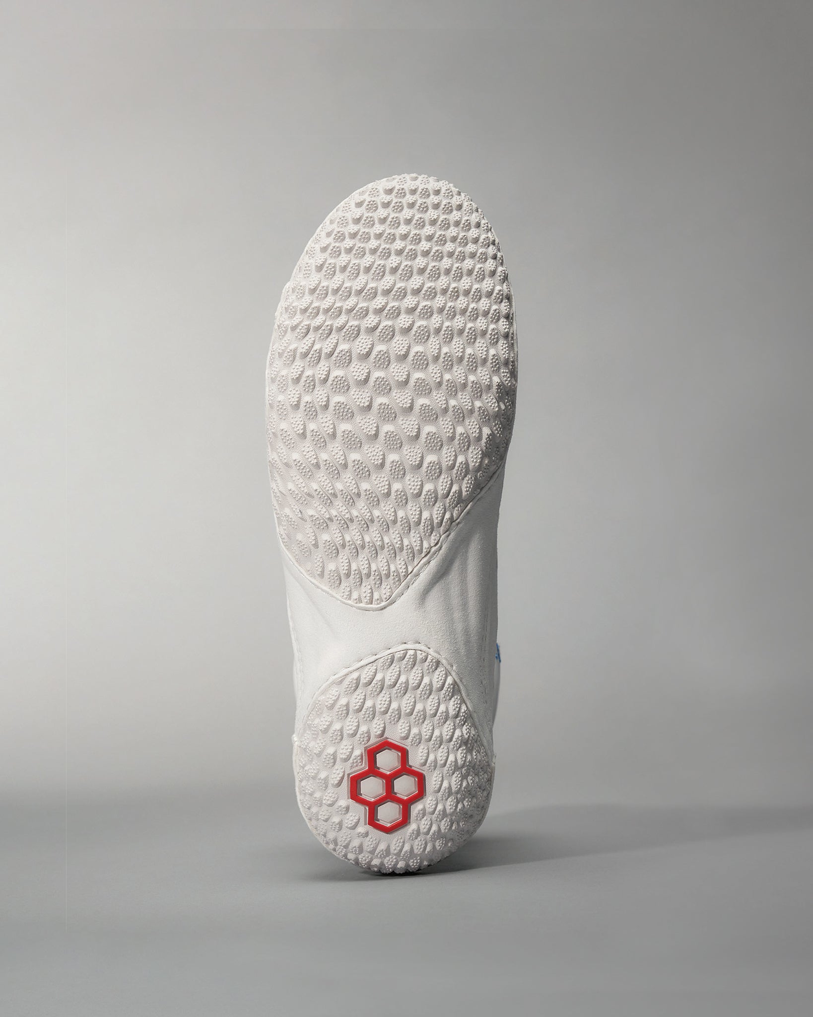 A close-up of the sole of a white athletic shoe featuring a unique textured pattern for grip and a striking red logo