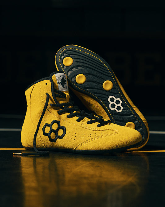 Yellow wrestling shoes with black accents on a dark background wrestling mat
