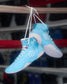 Blue wrestling shoes with white soles hanging from a bar in a boxing ring.