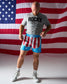 Man wearing a 'Rocky' t-shirt and American flag-themed shorts in front of an American flag.
