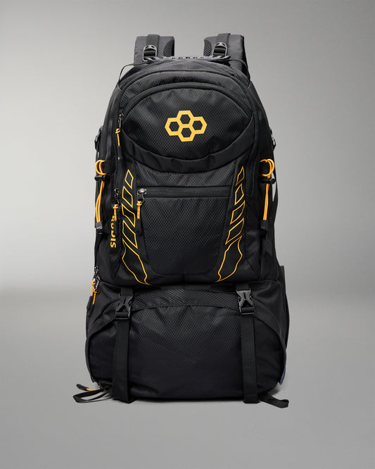 A black technical backpack with bright orange accents, including a geometric logo on the front pocket and vertical branding details, shown against a neutral gray background.