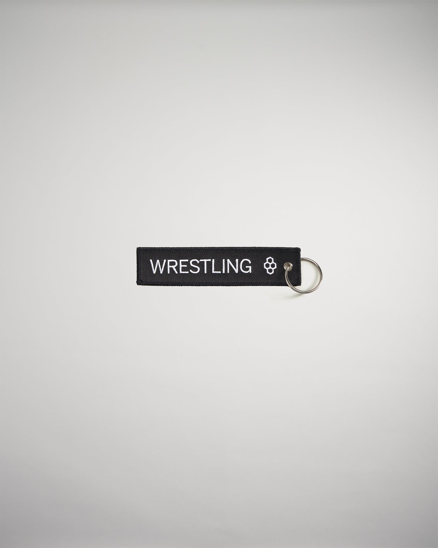 A black keychain tag featuring the word WRESTLING in bold white letters attached to a silver metal ring