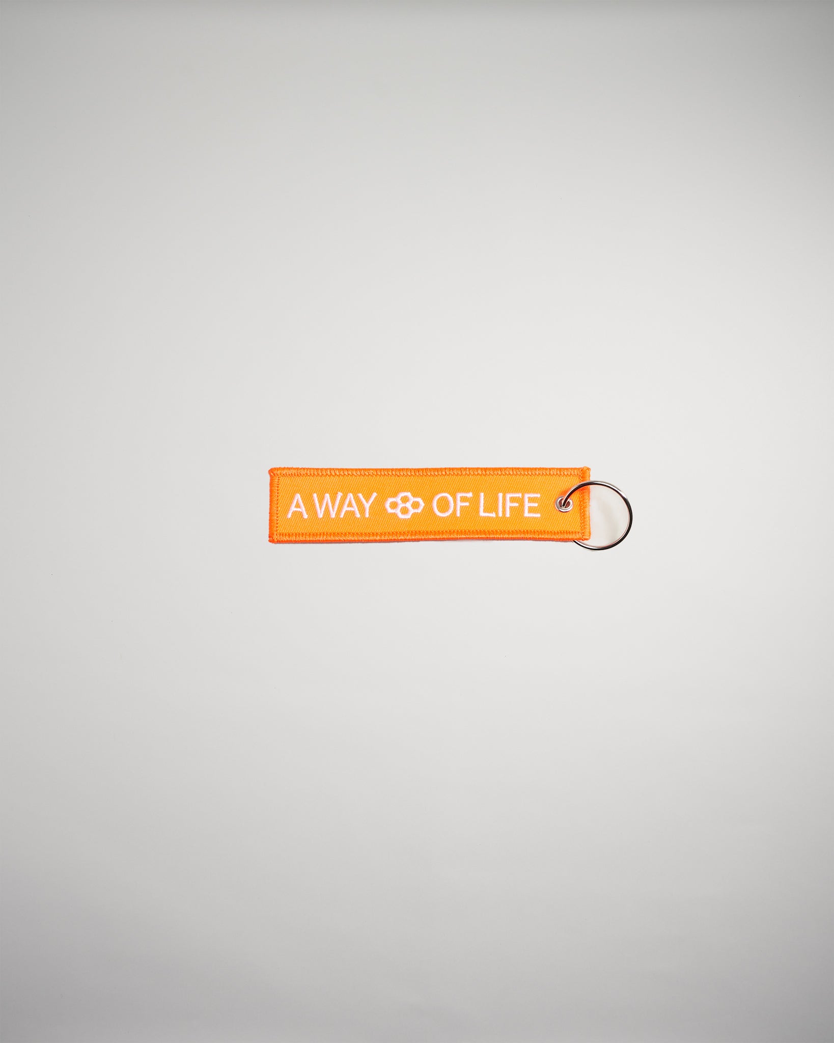 An orange fabric tag with the text A WAY OF LIFE displayed prominently attached to a metal keyring