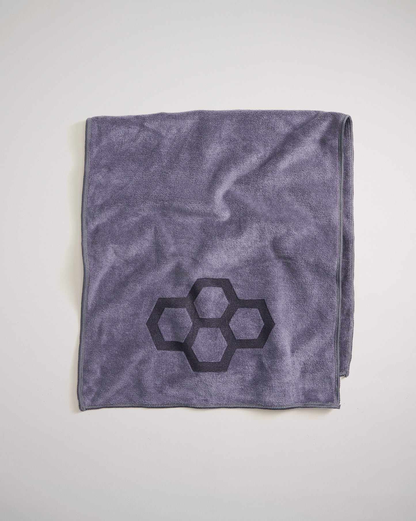 A folded purple towel featuring a geometric black honeycomb design in one corner