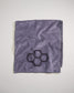 A folded purple towel featuring a geometric black honeycomb design in one corner