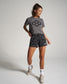 A young woman wearing a grey t-shirt with a geometric design and black camo shorts stands gracefully showcasing a casual athletic look