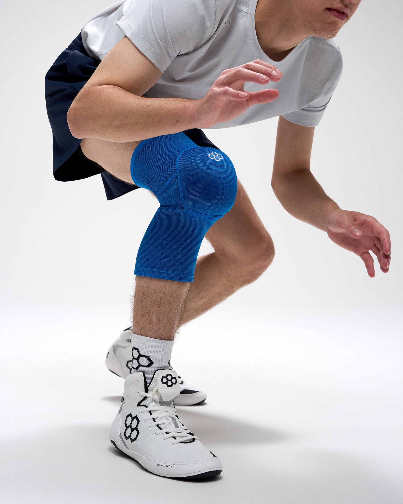 Person wearing blue knee pads and white athletic shoes on a plain background