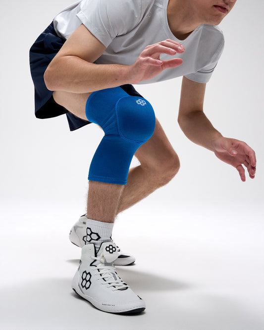 Person wearing blue knee pads and white athletic shoes on a plain background