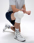 Person wearing a white knee pad and white sneakers with a quadhex design on a white background