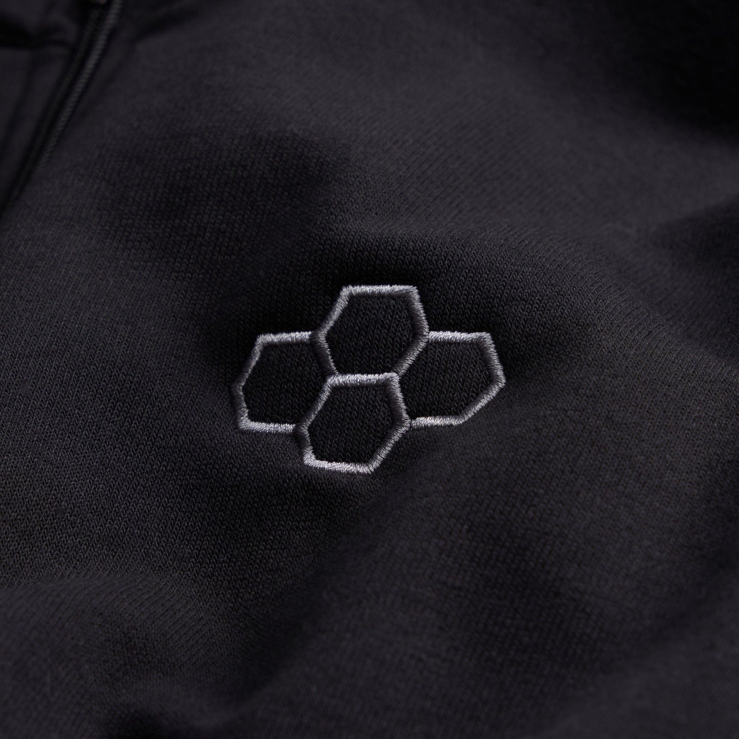 This image features a close-up of a black fabric surface adorned with an embroidered hexagonal logo in a lighter gray tone showcasing a sleek and modern design aesthetic