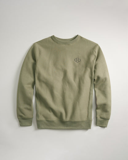 The image shows a cozy olive green sweatshirt featuring a minimalistic embroidered logo on the chest laid flat against a soft neutral background