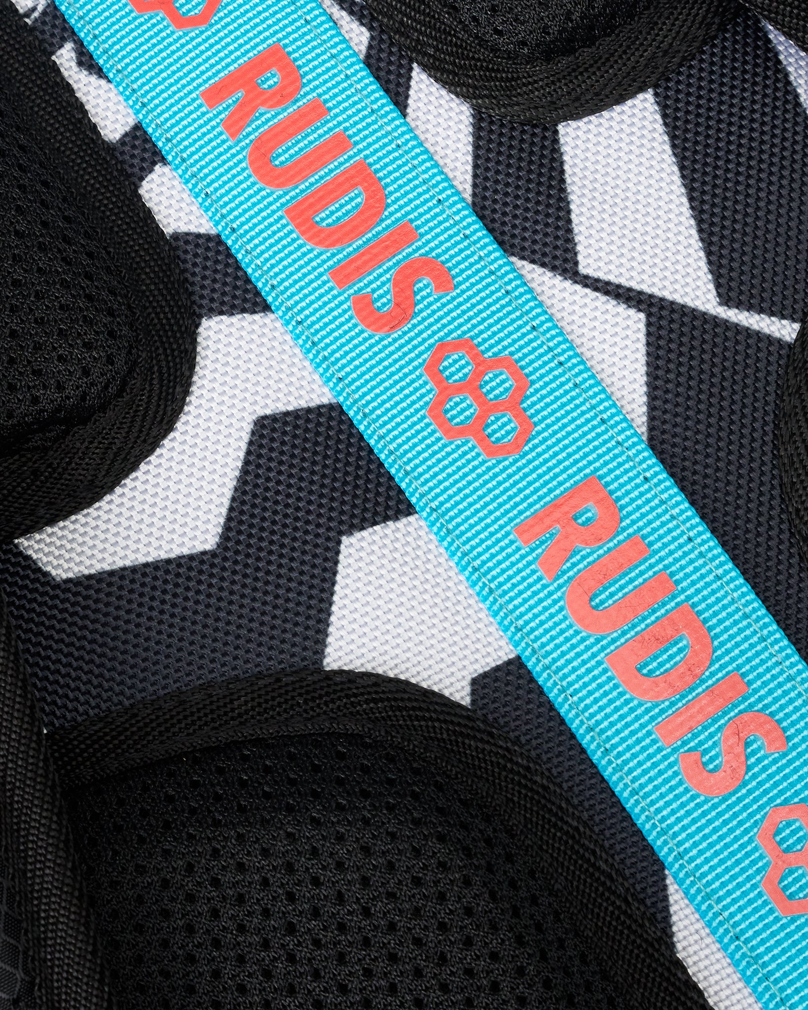 Close-up of a black and white geometric patterned textile with a bright turquoise strap printed repeatedly with the brand name RUDIS in coral.