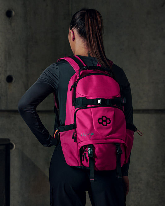 Person wearing a pink backpack with a logo on a dark background