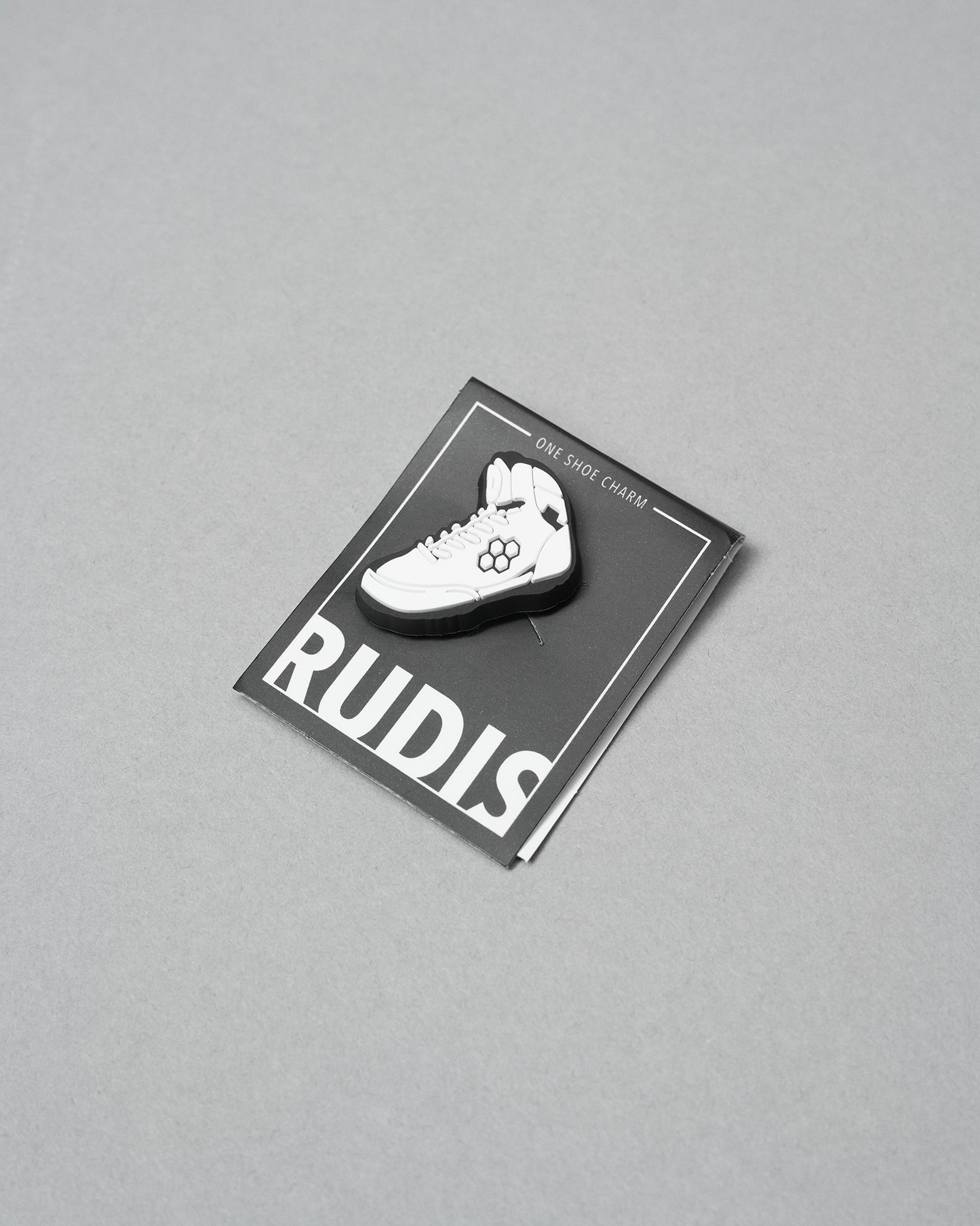 White shoe charm on a RUDIS branded card against a gray background