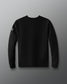 The back view of a black crewneck sweatshirt is shown against a gray background. The sweatshirt has a clean, minimal design with no graphics on the back. A small white RUDIS hex logo is visible on the upper right sleeve near the shoulder.