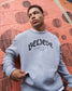 Person wearing a gray sweatshirt with 'BELIEVE' text against a red and orange wall.