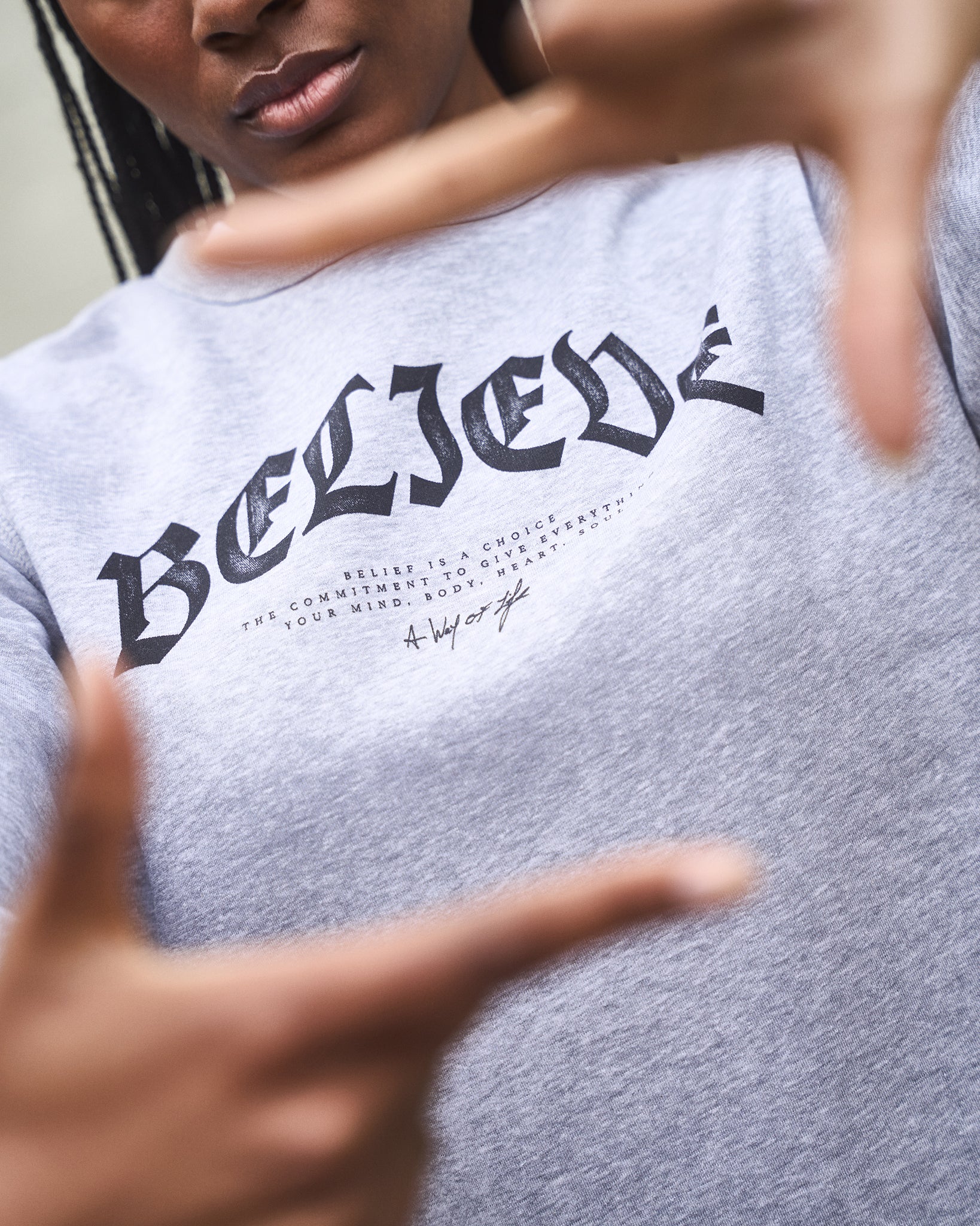 Person wearing a gray sweatshirt with 'BELIEVE' printed on it, pointing at the text.