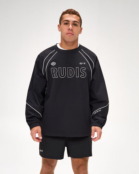 A man modeling a black long-sleeve athletic sweatshirt with white piping and 'RUDIS' printed across the chest, paired with matching black shorts against a light gray studio background.