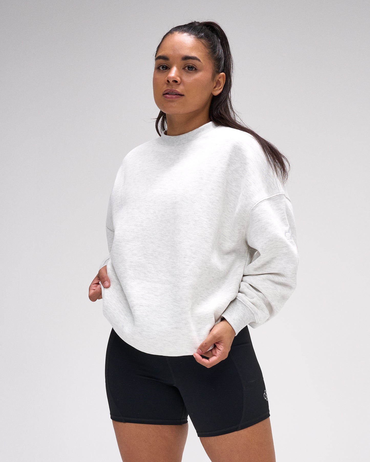 Woman wearing a white sweatshirt and black shorts on a plain background