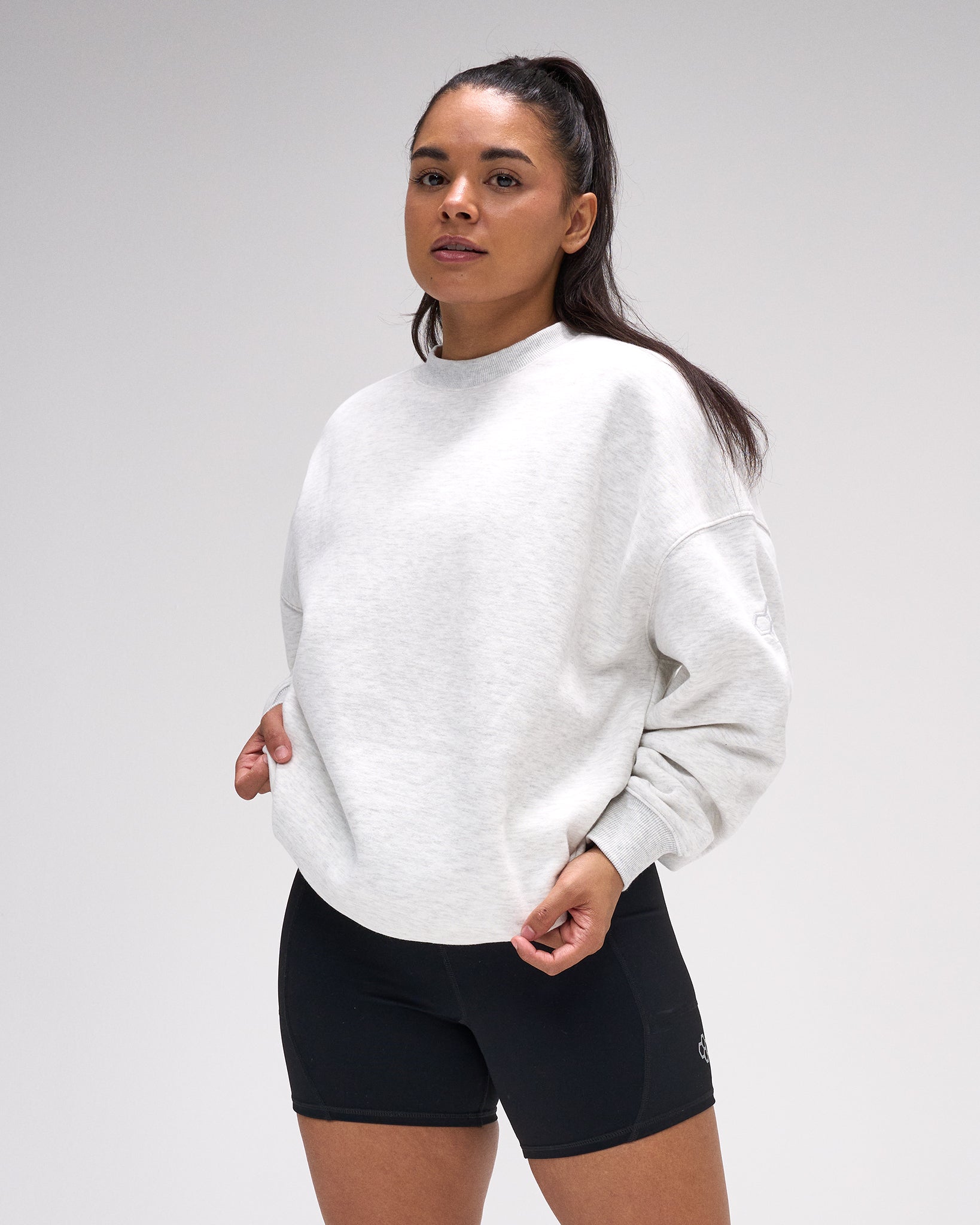 Woman wearing a white sweatshirt and black shorts on a plain background