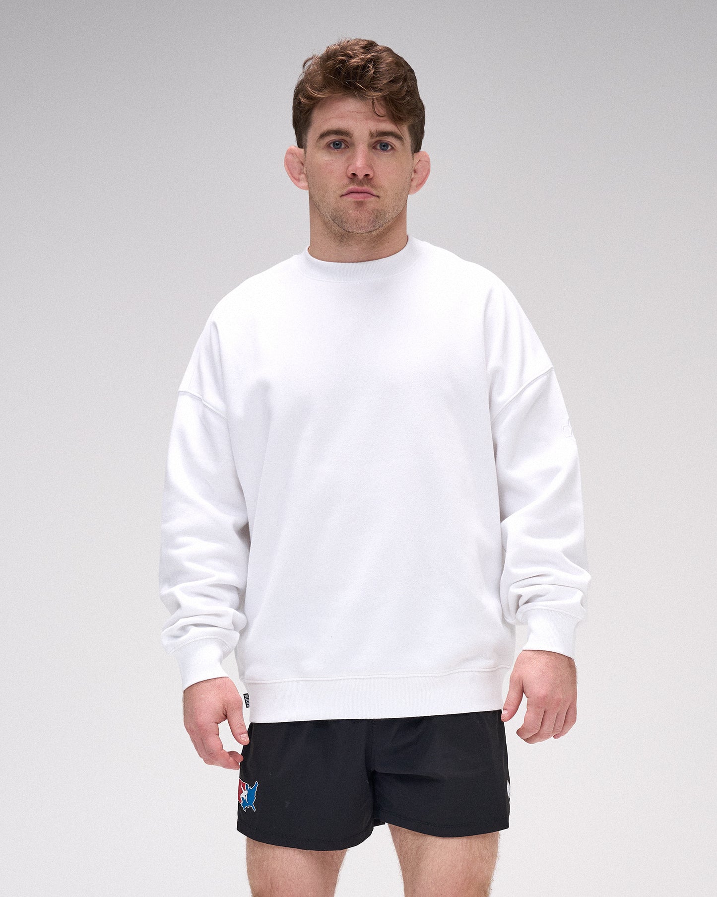 Man wearing a white sweatshirt and black shorts on a gray background