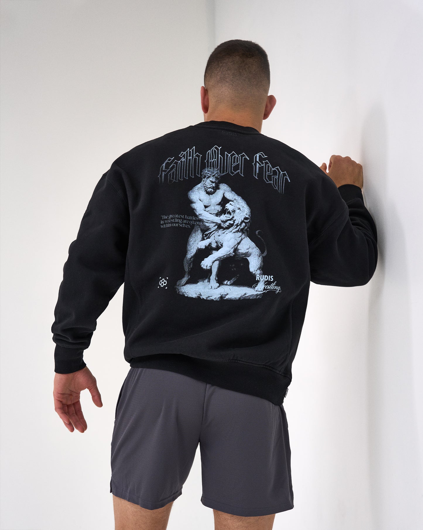 Person wearing a black sweatshirt with a graphic design on the back, standing against a white wall.