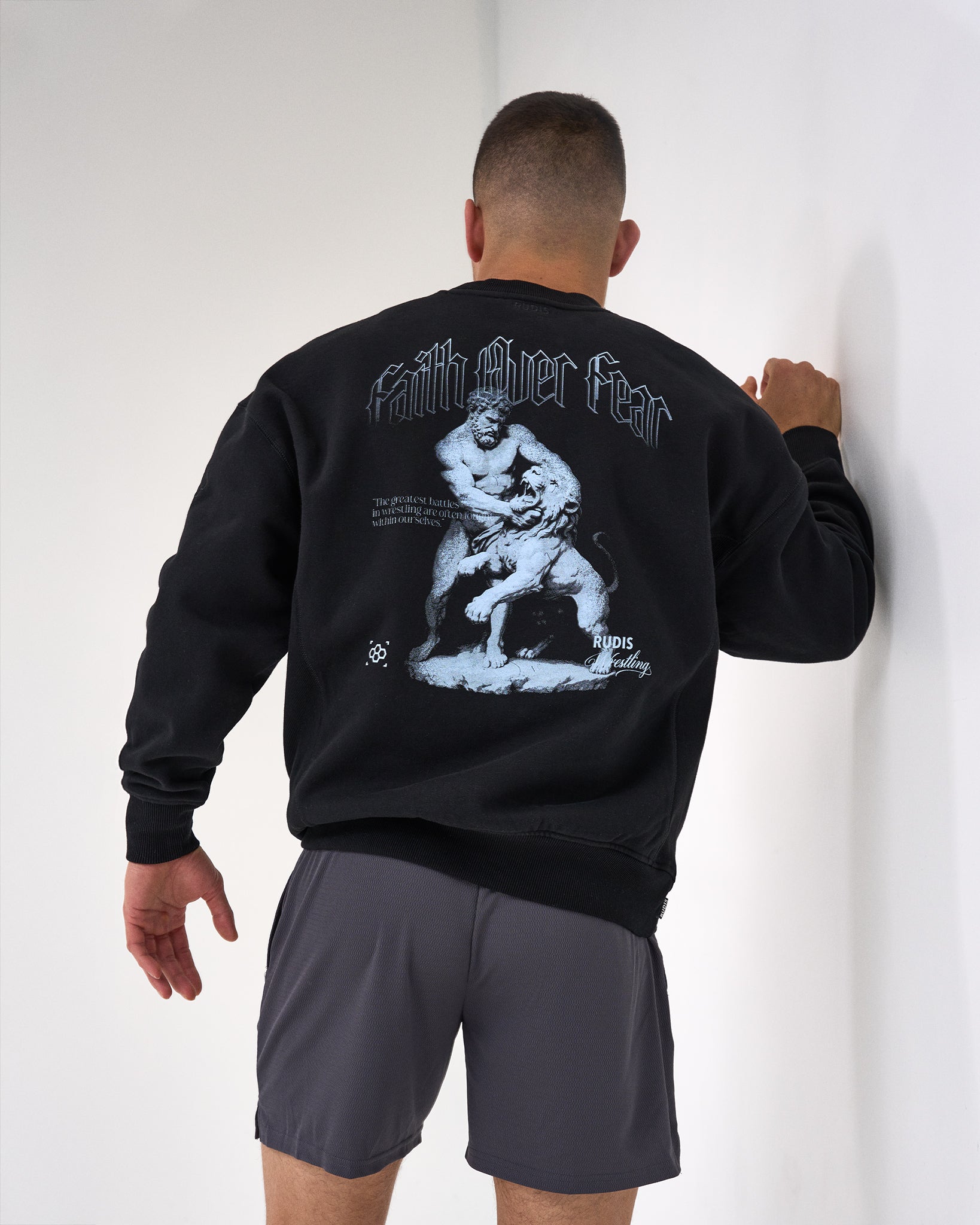 Person wearing a black sweatshirt with a graphic design on the back, standing against a white wall.
