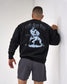 Person wearing a black sweatshirt with a graphic design on the back, standing against a white wall.