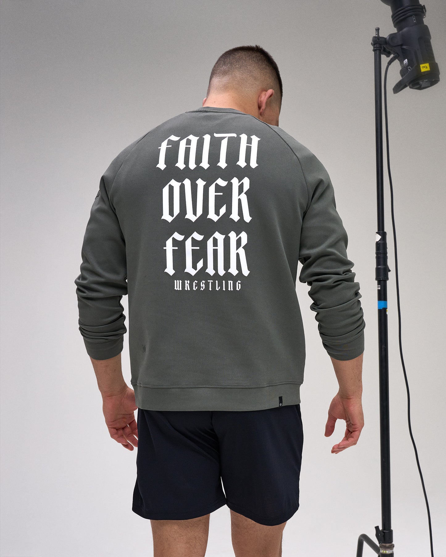 Person wearing a gray sweatshirt with 'Faith Over Fear Wrestling' text on the back, standing against a plain background.