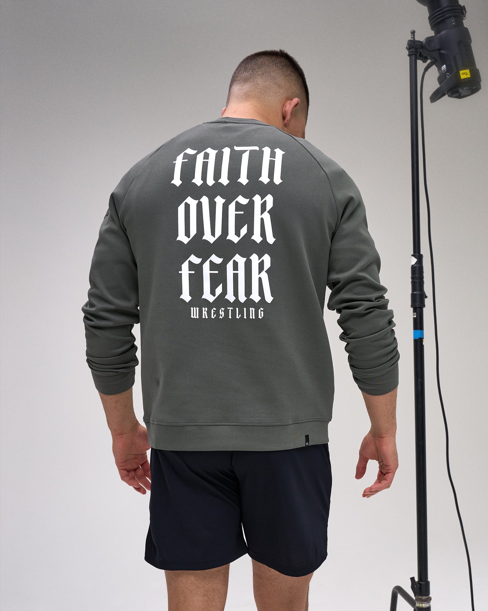 Person wearing a gray sweatshirt with 'Faith Over Fear Wrestling' text on the back, standing against a plain background.