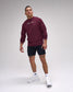 Man wearing a maroon sweatshirt with text, black shorts, white socks, and sneakers on a gray background
