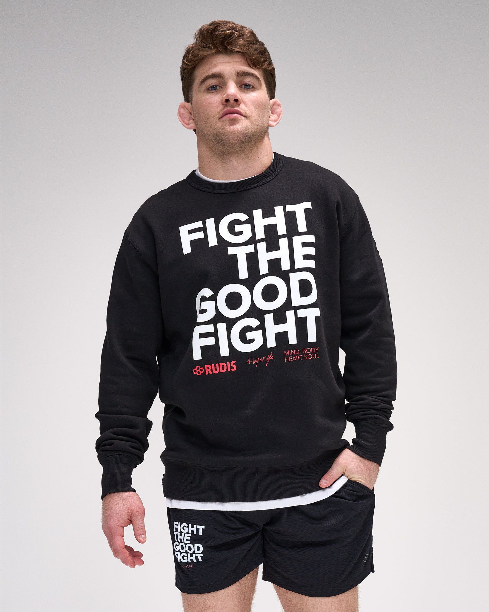 Man wearing a black crewneck with 'Fight The Good Fight' text on a gray background