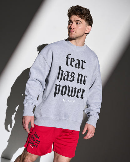 Man wearing a gray crewneck with 'fear has no power' text and red shorts with similar text, standing against a white and black background.