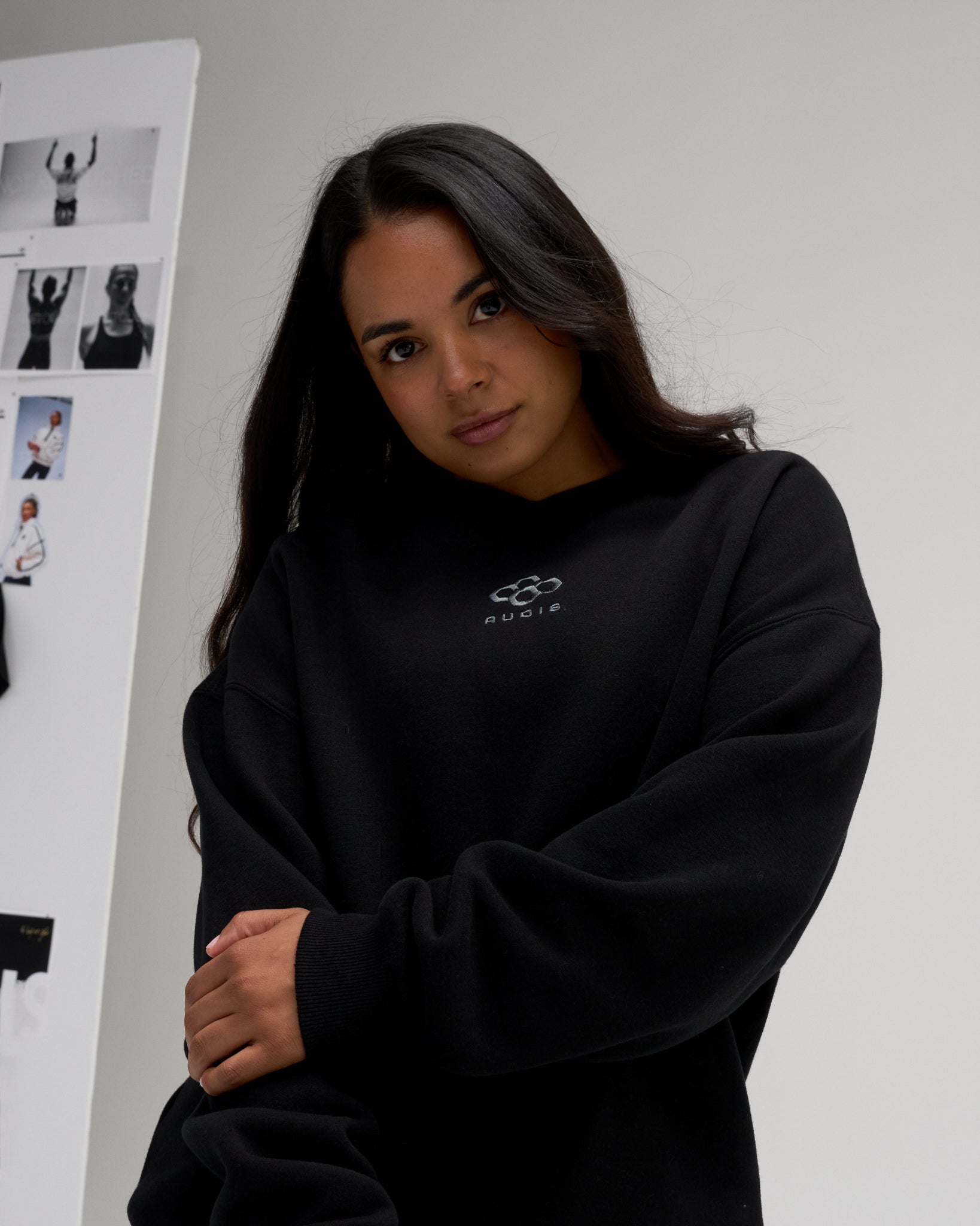 Woman modeling the RUDIS Hex Relaxed Comfort Fleece Crewneck in Black, highlighting the subtle chest logo, dropped shoulders, and ribbed cuffs.
 Copy alt text