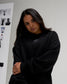 Woman modeling the RUDIS Hex Relaxed Comfort Fleece Crewneck in Black, highlighting the subtle chest logo, dropped shoulders, and ribbed cuffs.
 Copy alt text