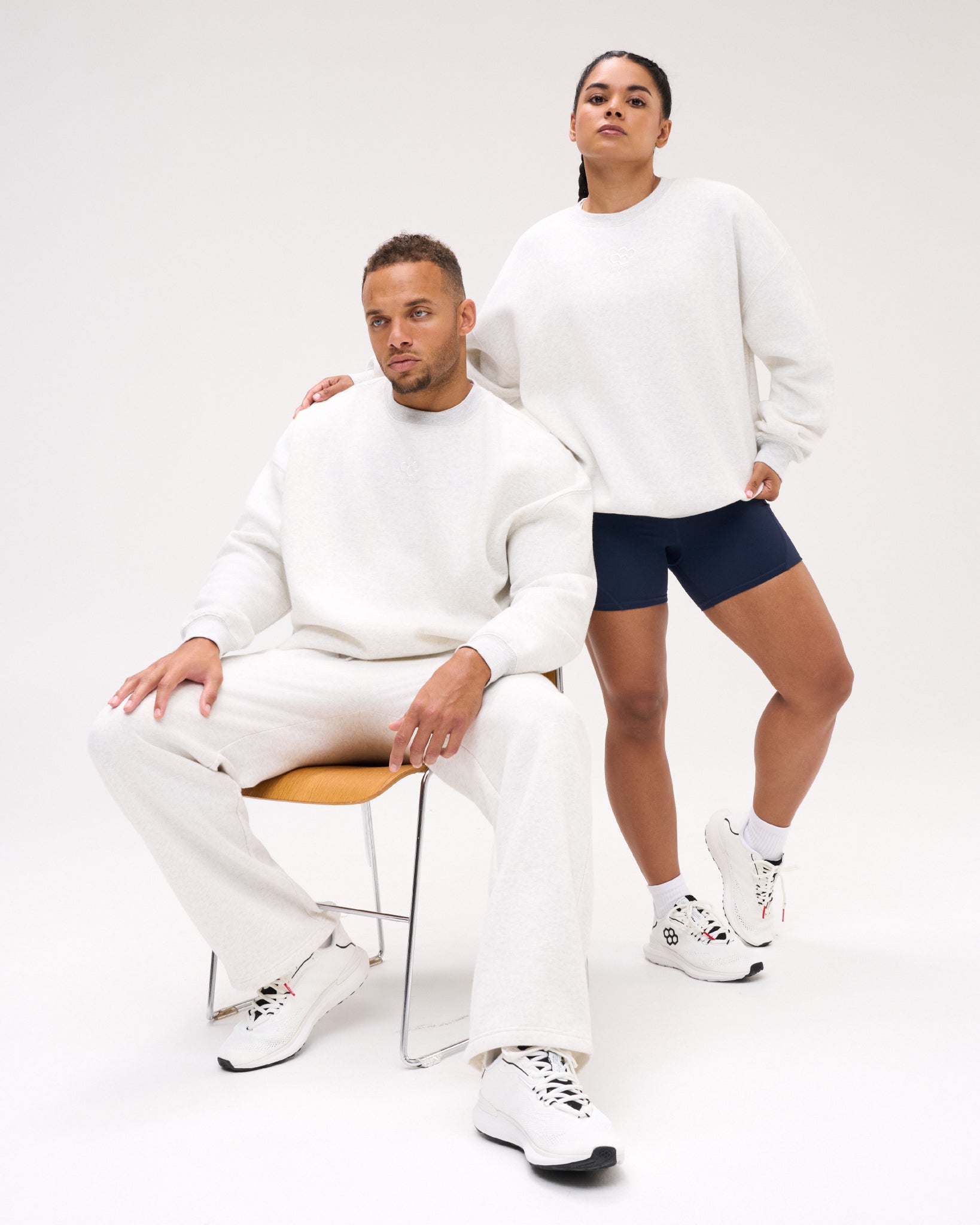 Male and female models wearing the RUDIS Hex Relaxed Comfort Fleece Crewneck in Heather Silver, featuring tonal hex branding and a relaxed fit.
 Copy alt text