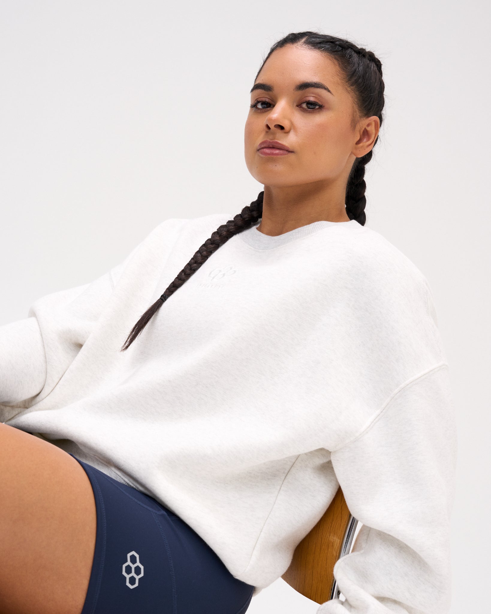 Woman wearing the RUDIS Hex Relaxed Comfort Fleece Crewneck in Heather Silver with a subtle chest logo, dropped shoulders, and ribbed neckline.
 Copy alt text