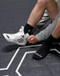 Person wearing a white wrestling shoe with black accents on a dark surface.