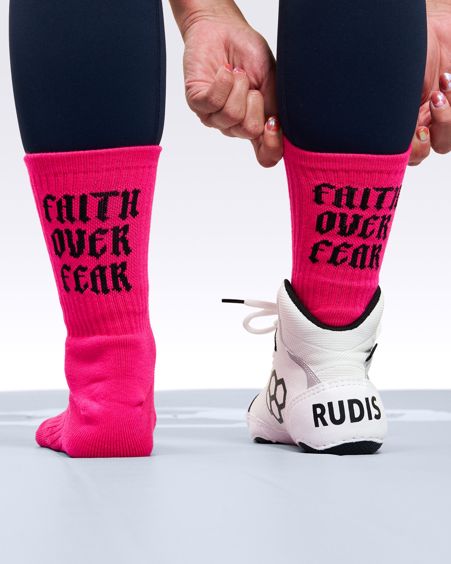 Person wearing bright pink socks with 'Faith Over Fear' text, black leggings, and white sneakers on a light background.