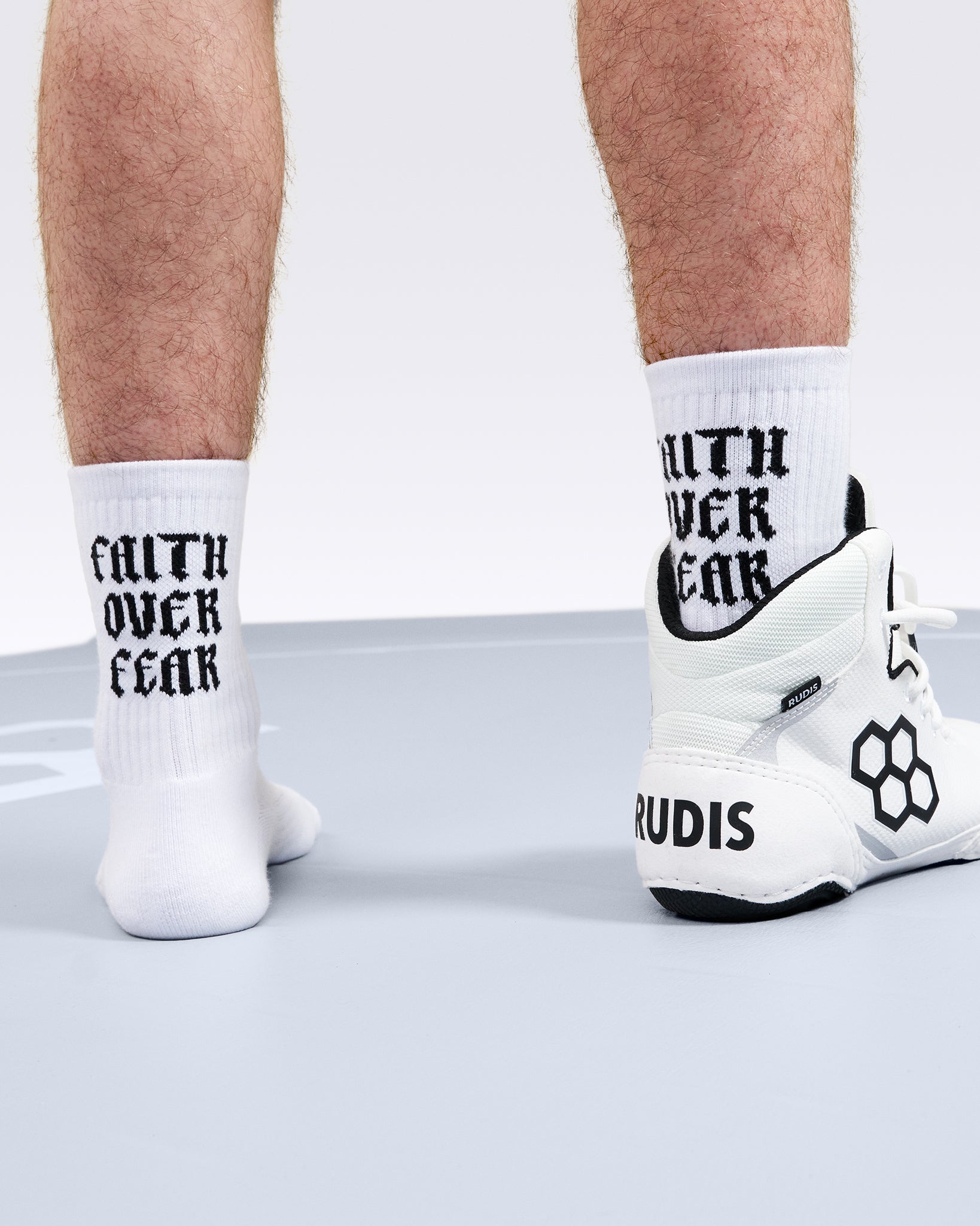 Person wearing white socks with 'Faith Over Fear' text and white sneakers on a light background