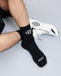 Person wearing black socks with a logo and 'RUDIS' text, paired with a white sneaker on a light gray background.