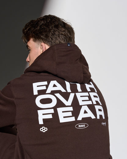 Person wearing a brown hoodie with 'Faith Over Fear' text on the back, standing against a neutral background.
