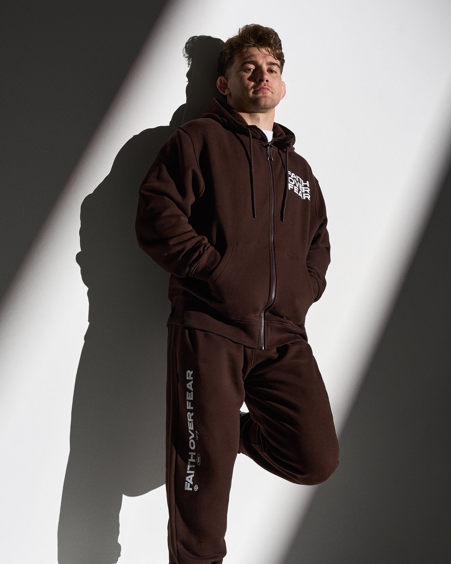 Person wearing a brown sweatsuit with visible branding against a white and gray background