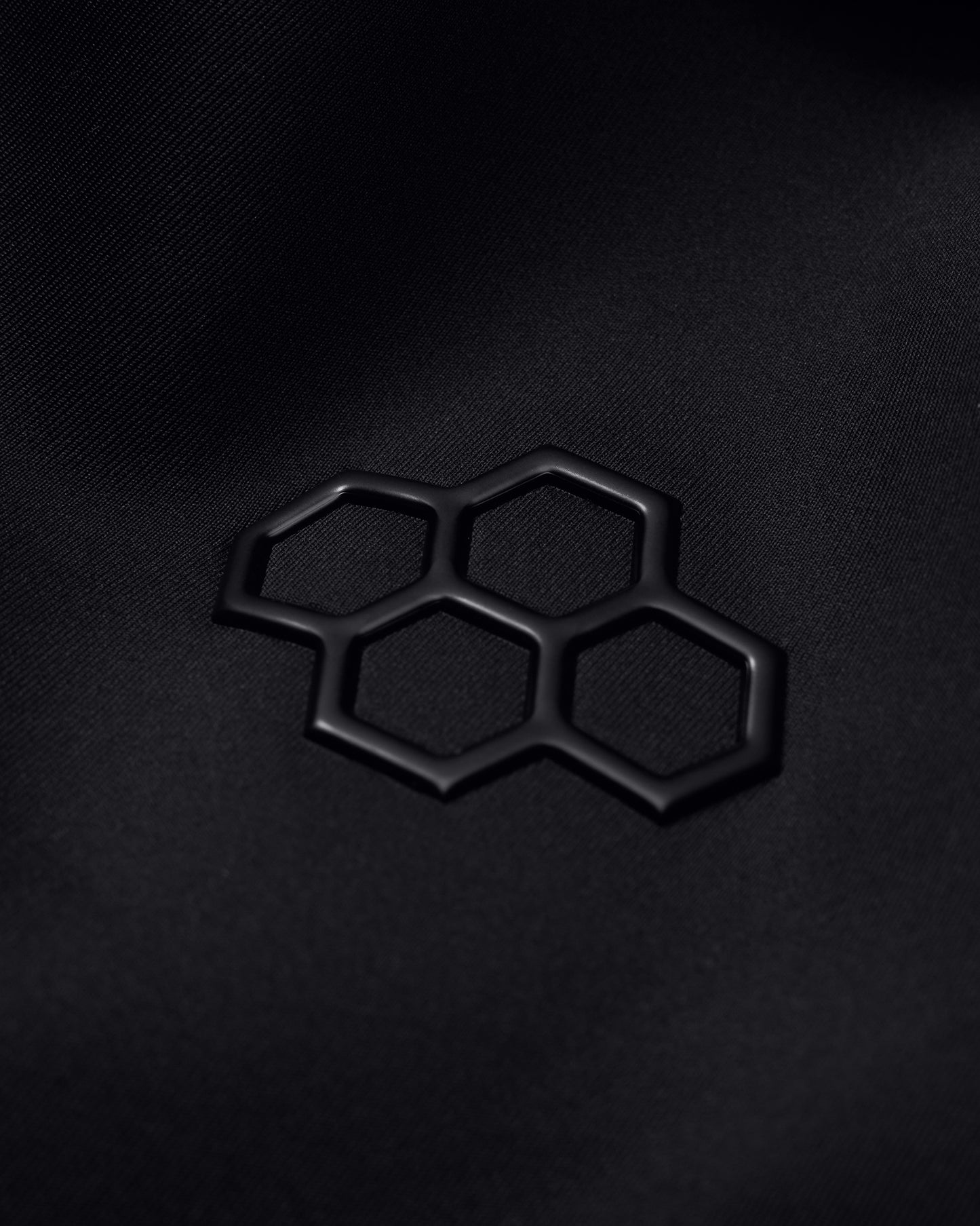 A black fabric surface with a subtly textured appearance showcases a raised darker hexagonal logo, emphasizing modern design.