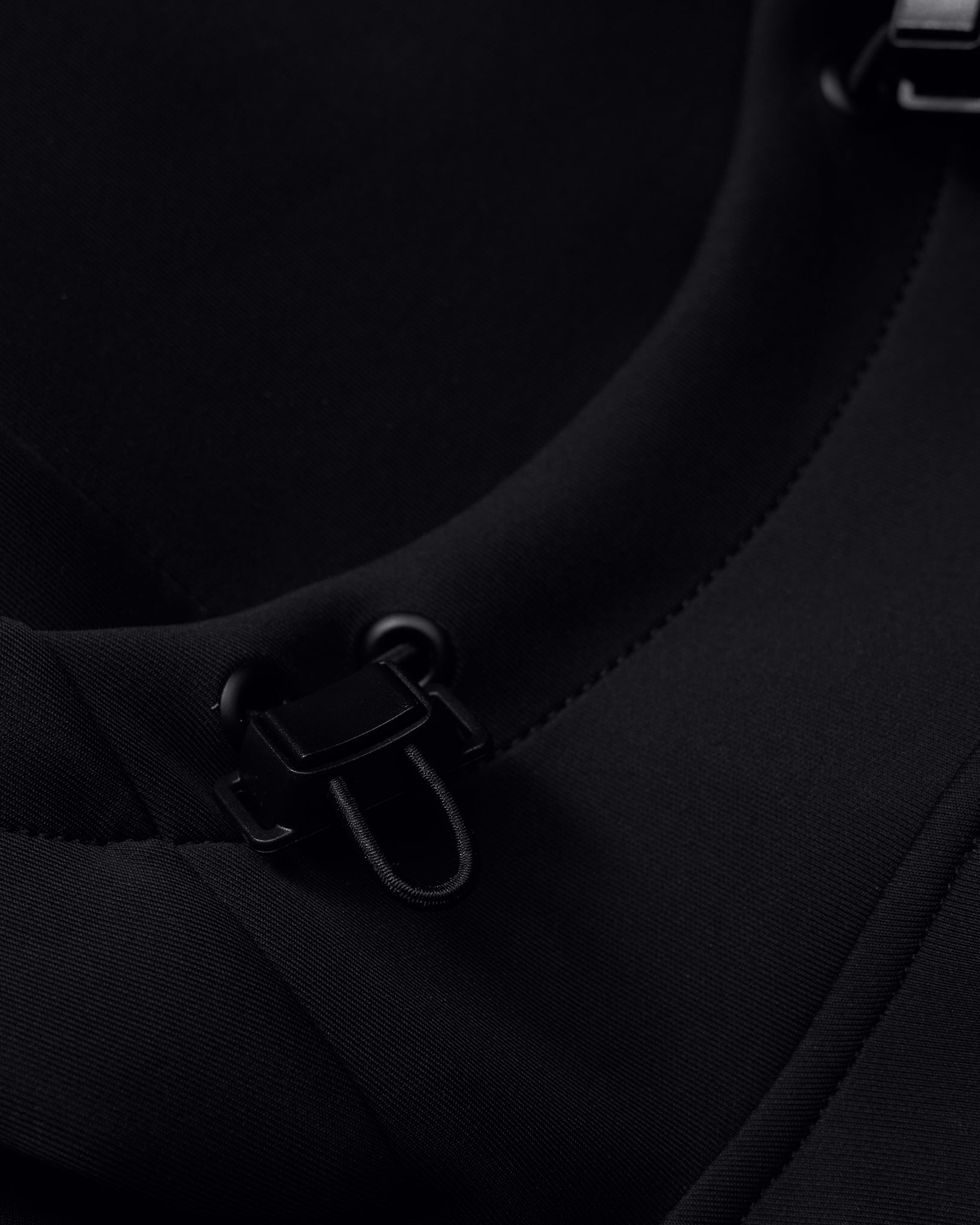 Close-up view of a black fabric featuring fastening elements and detailed stitching, showcasing practical design for active wear.