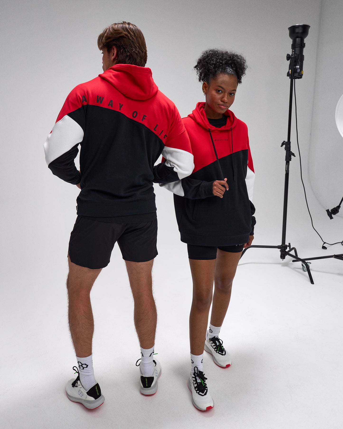 Two people wearing matching red and black hoodies in a studio setting.