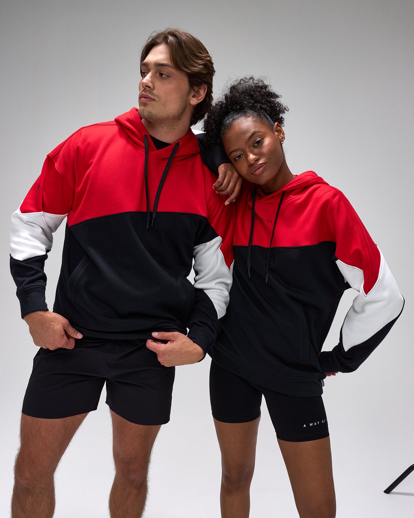 Two people wearing matching red, black, and white hoodies and shorts on a gray background