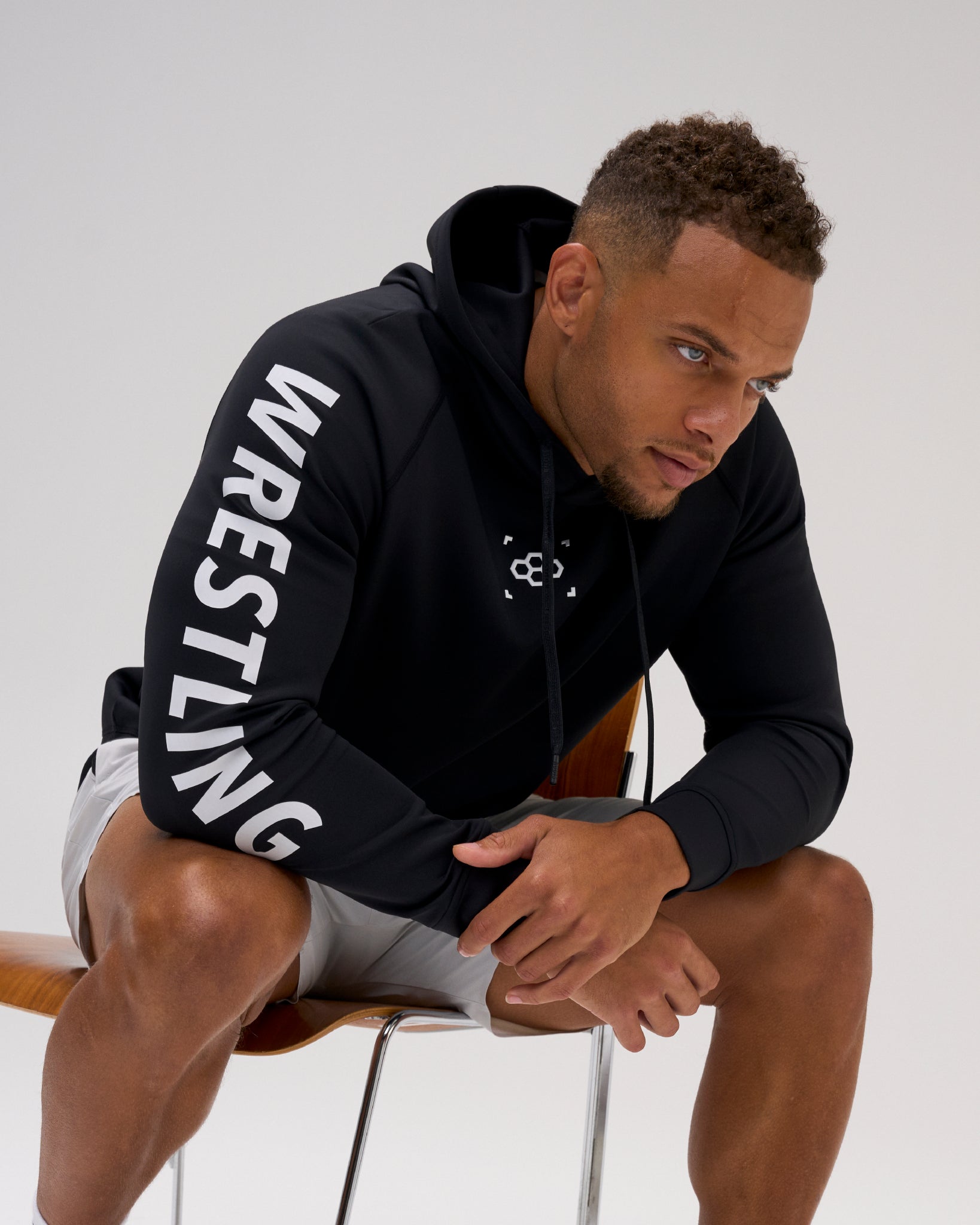 Male athlete wearing the black RUDIS Wrestling COOL-FEEL Hoodie while seated, highlighting the white WRESTLING sleeve graphic and RUDIS chest mark.